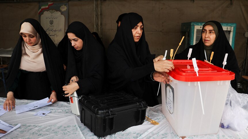 Four women are preparing a ballot box ahead of an election.