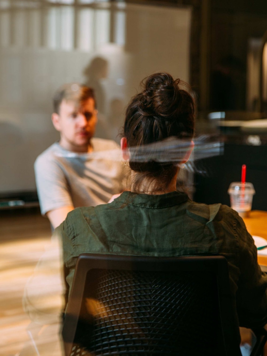 A woman and a man sit face to face in a cafe.