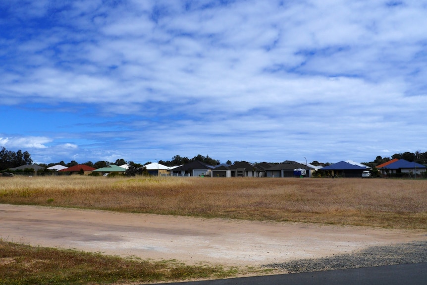 A vacant land under blue sky, housing can be seen in the distance.