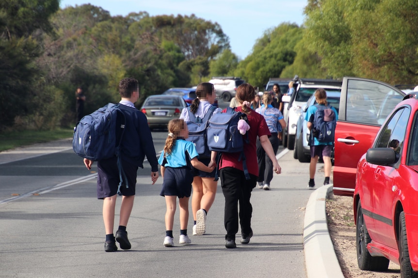 Children in school uniform walking along a road with parents