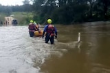 Three fire and rescue personnel ferry a child through flood waters on a raft