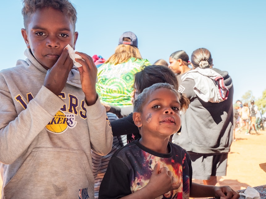 Two young boys wipe their faces in front of red dirt