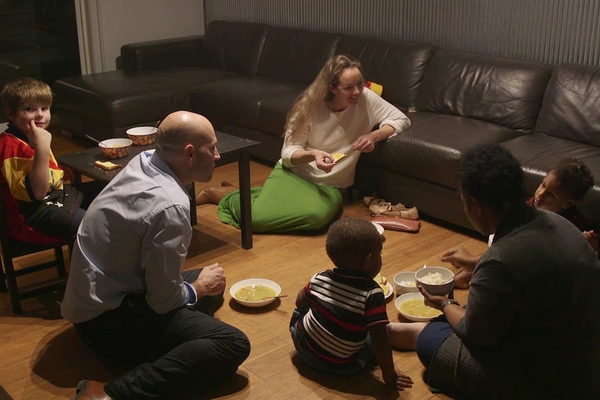 The Shearmans and Michelle Tanga Uri sitting on the lounge room floor eating dinner