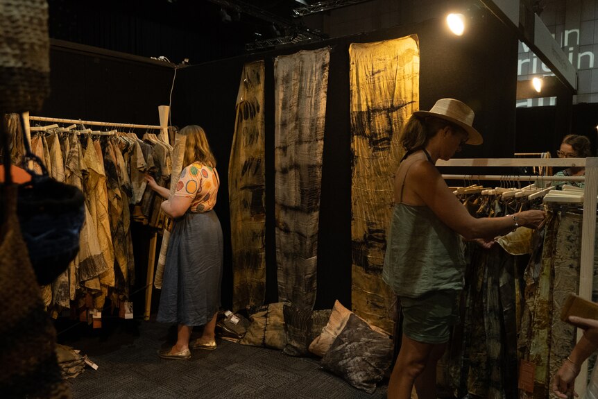 Two women look through fabrics hung on racks inside an art gallery.