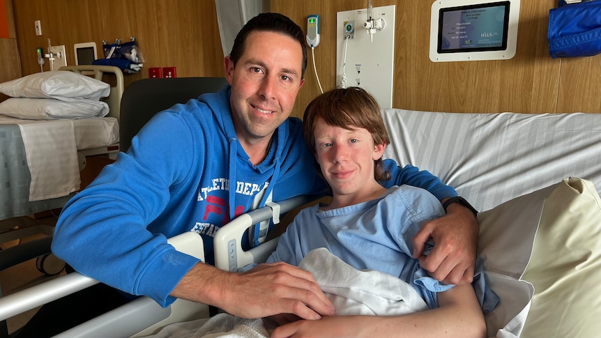 A man wraps his arms around a boy in a hospital bed.