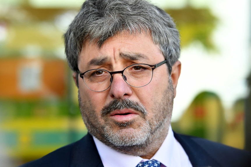 A close up shot of Brisbane barrister Sam Di Carlo wearing a suit and glasses.