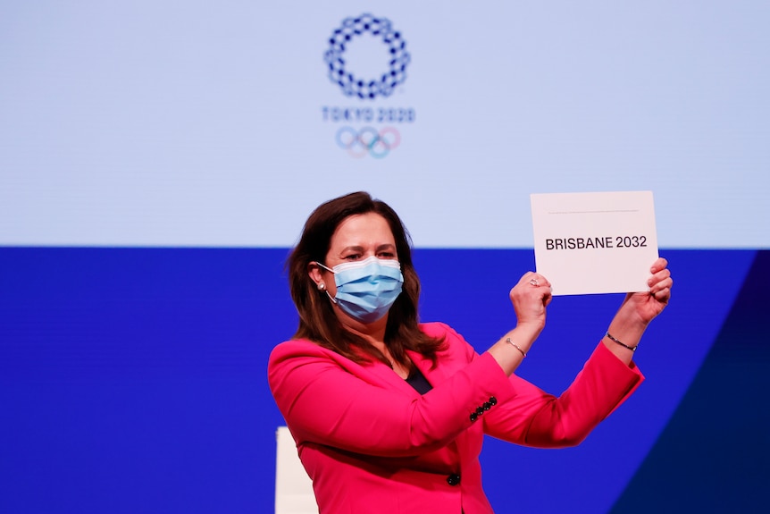 Woman wearing a pink jackets holds a sign which says Brisbane 2032