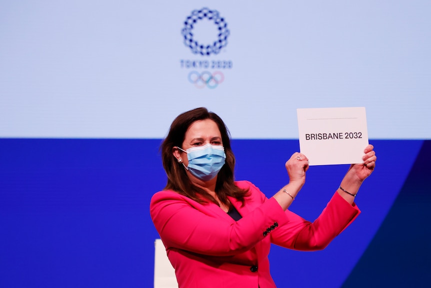 A woman wearing a pink jackets holds a sign that says "Brisbane 2032".