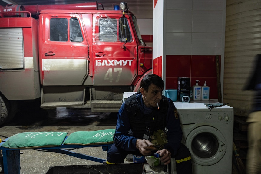 A Ukrainian firefighter smokes a cigarette at a fire station sitting in front of a fire truck