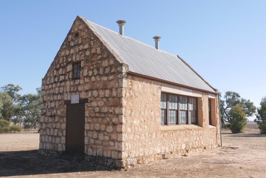 A small yellow sandstone building stands on a dusty clearing 