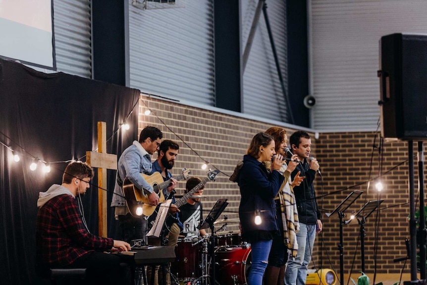 Seven musicians perform worship songs from an raised stage in a school gym.