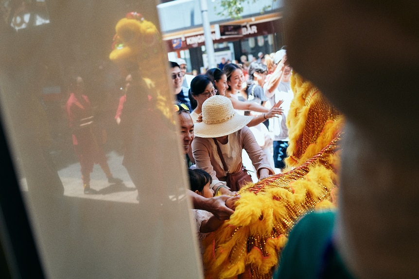 A yellow Chinese dragon watched by smiling onlookers.