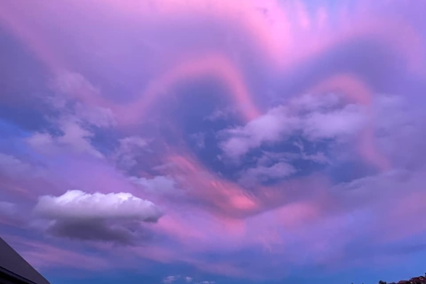 Pink and purple clouds form the shape of a heart in the sky.