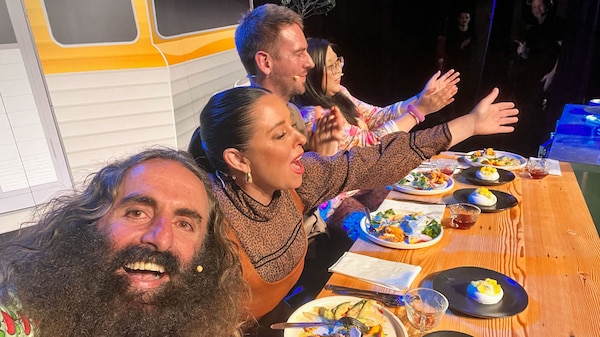 Costa and Myf at a table in front of a caravan eating dinner.