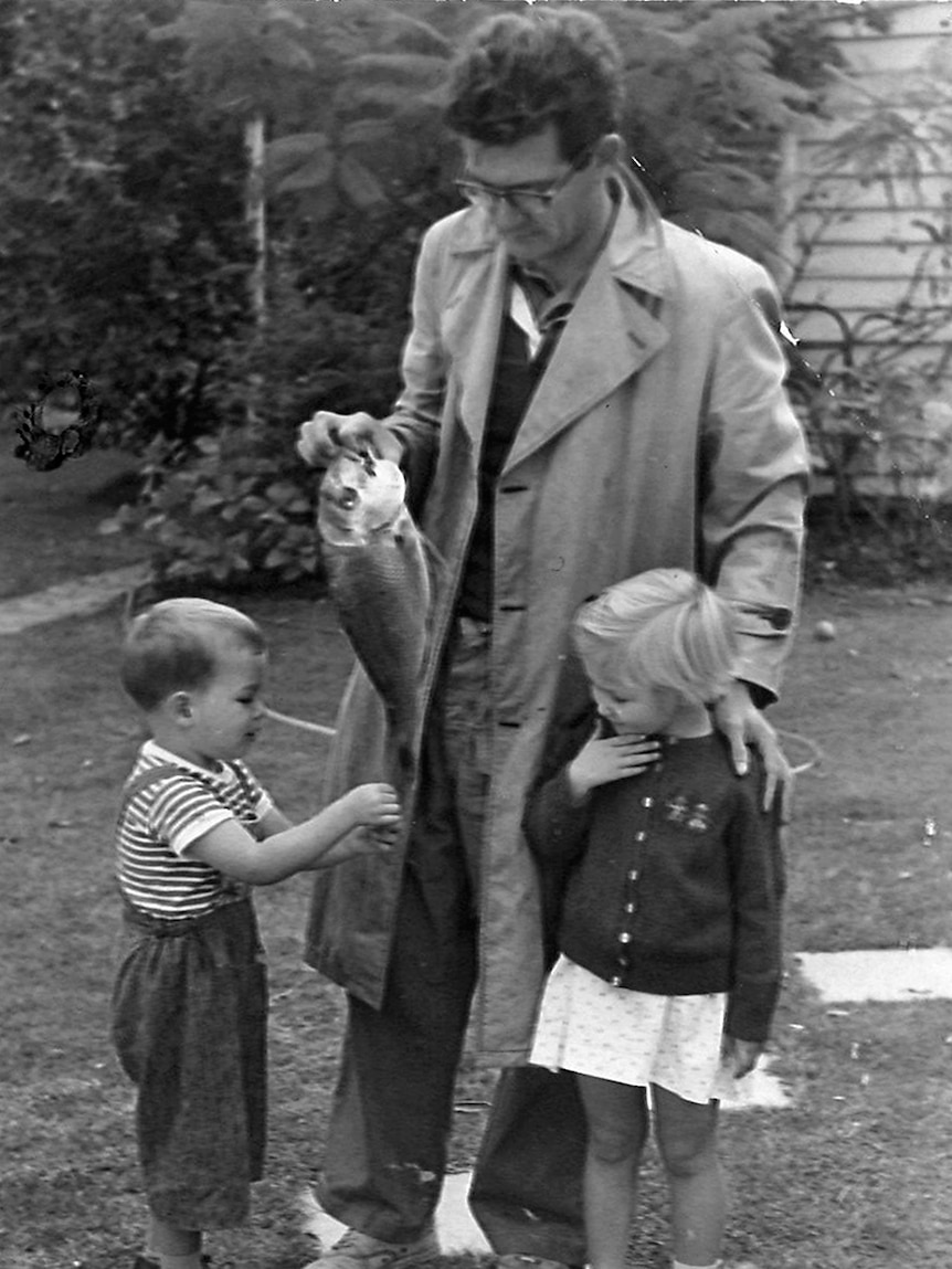 Bob Hawke holds a fish and stands with two small children.