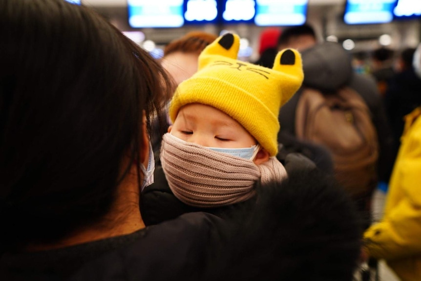 A child with a face mask held on a woman's arm.