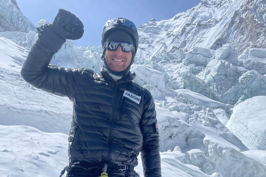 A man dressed in snow gear, in the snow, raises a fist in triumph