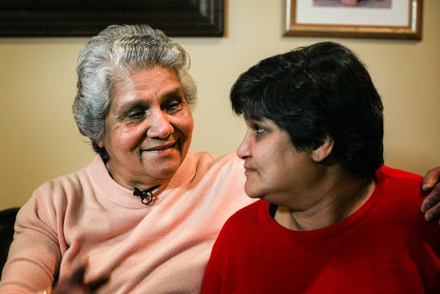 An elderly Indian woman smiles at her middle-aged daughter.