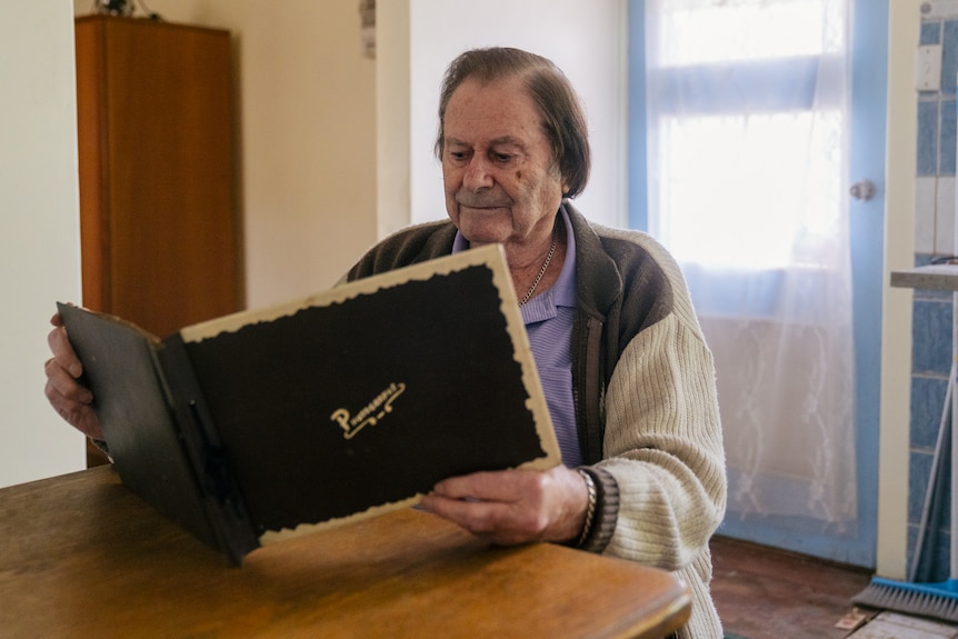 A man sits at a dinner table indorrs looking at a photo album.