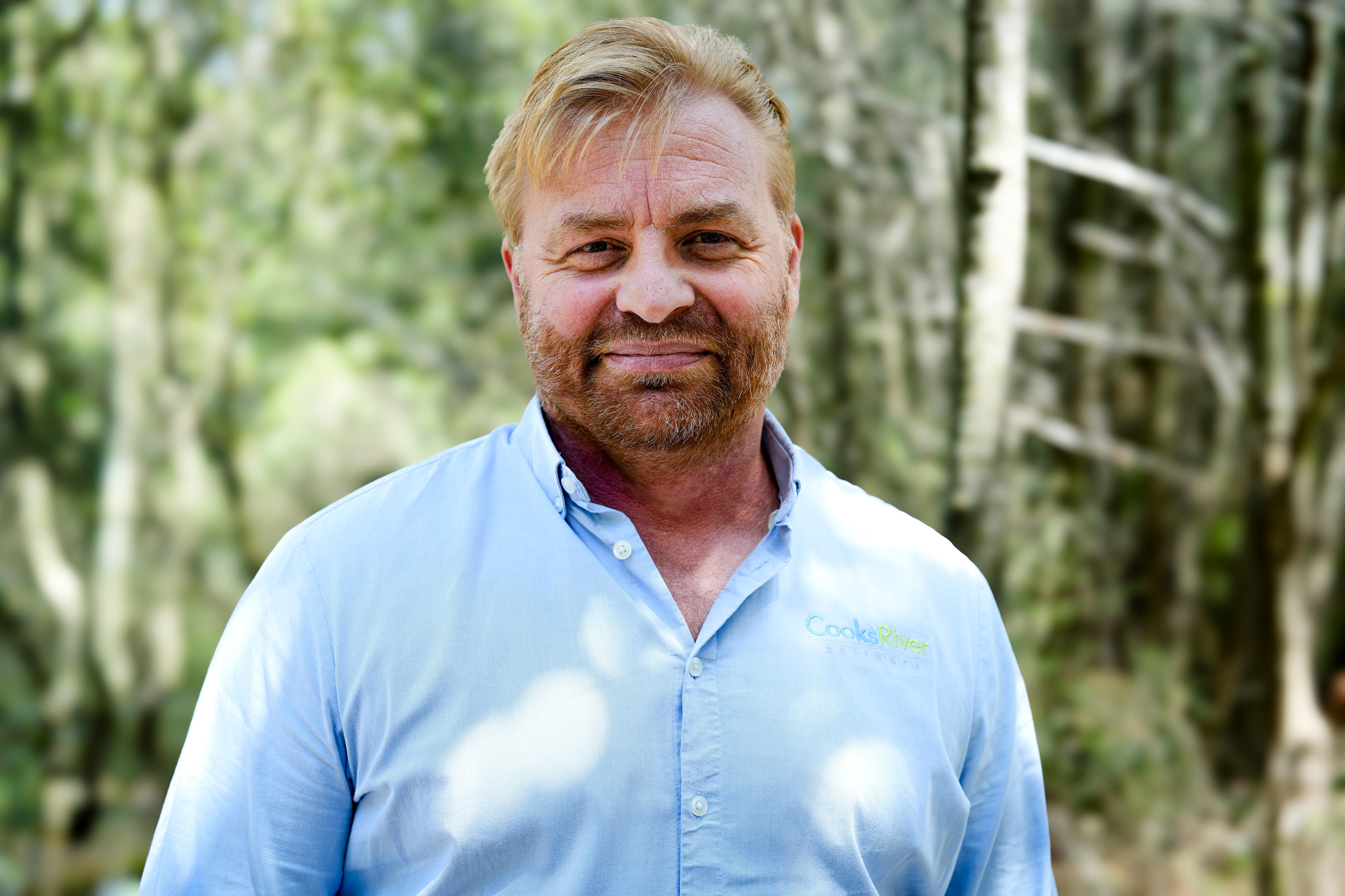 El Dr. Thomas sonríe a la cámara y se para frente a los árboles.