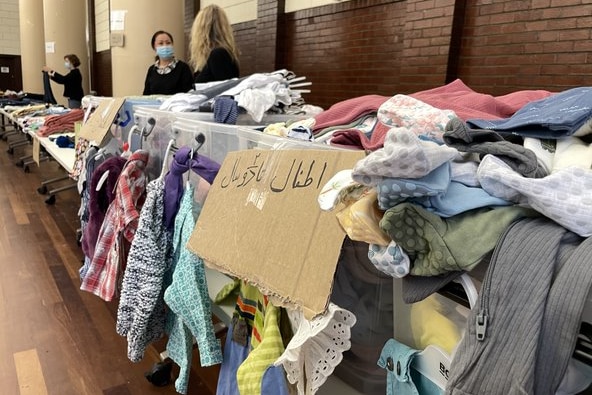 A table filled with clothes, with a label written in Arabic letters to alert refugees.