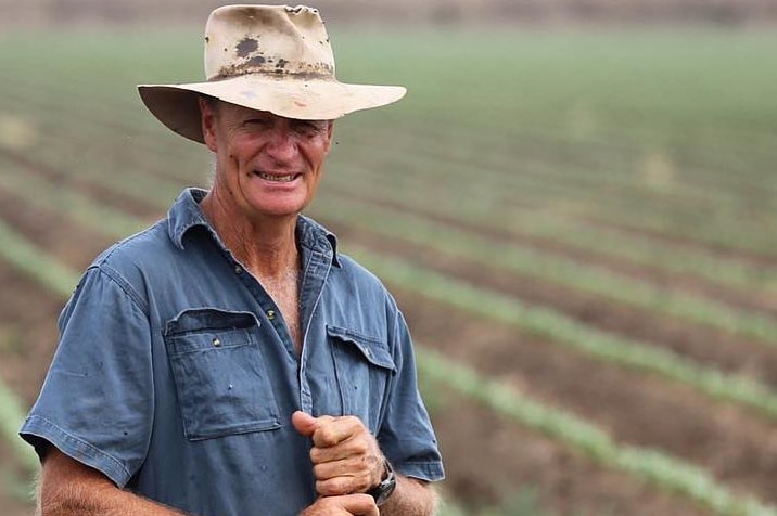 Farmer stands in field with battered hat