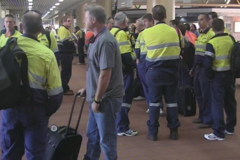 Men in hi-vis stand with suitcases in an airport terminal.