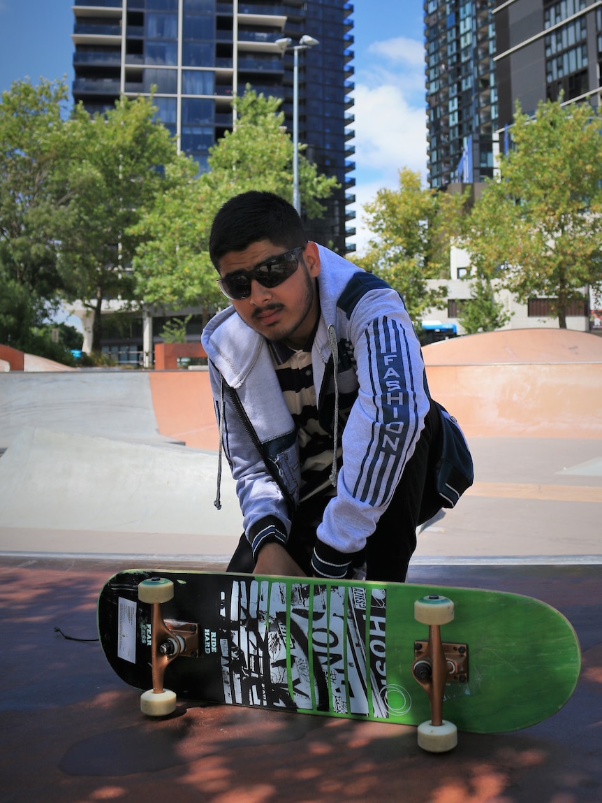 Teenage boy wearing sunglasses holding a skateboard. 