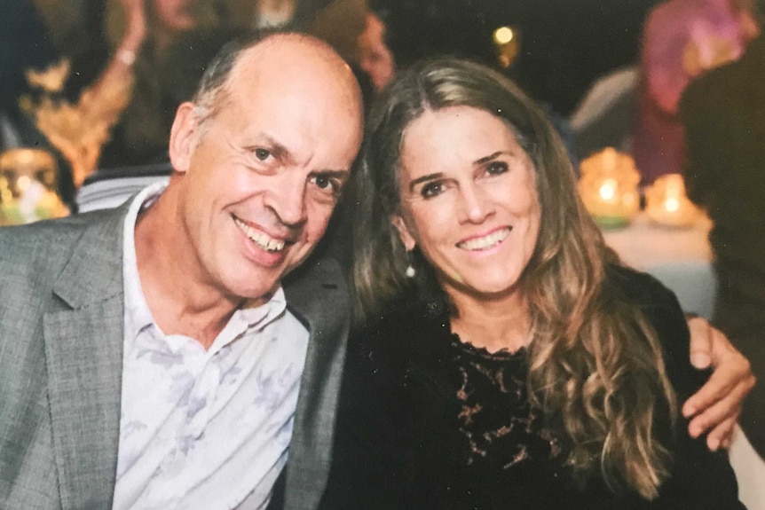 A couple smile and hug sitting at a dining table at a dinner function.