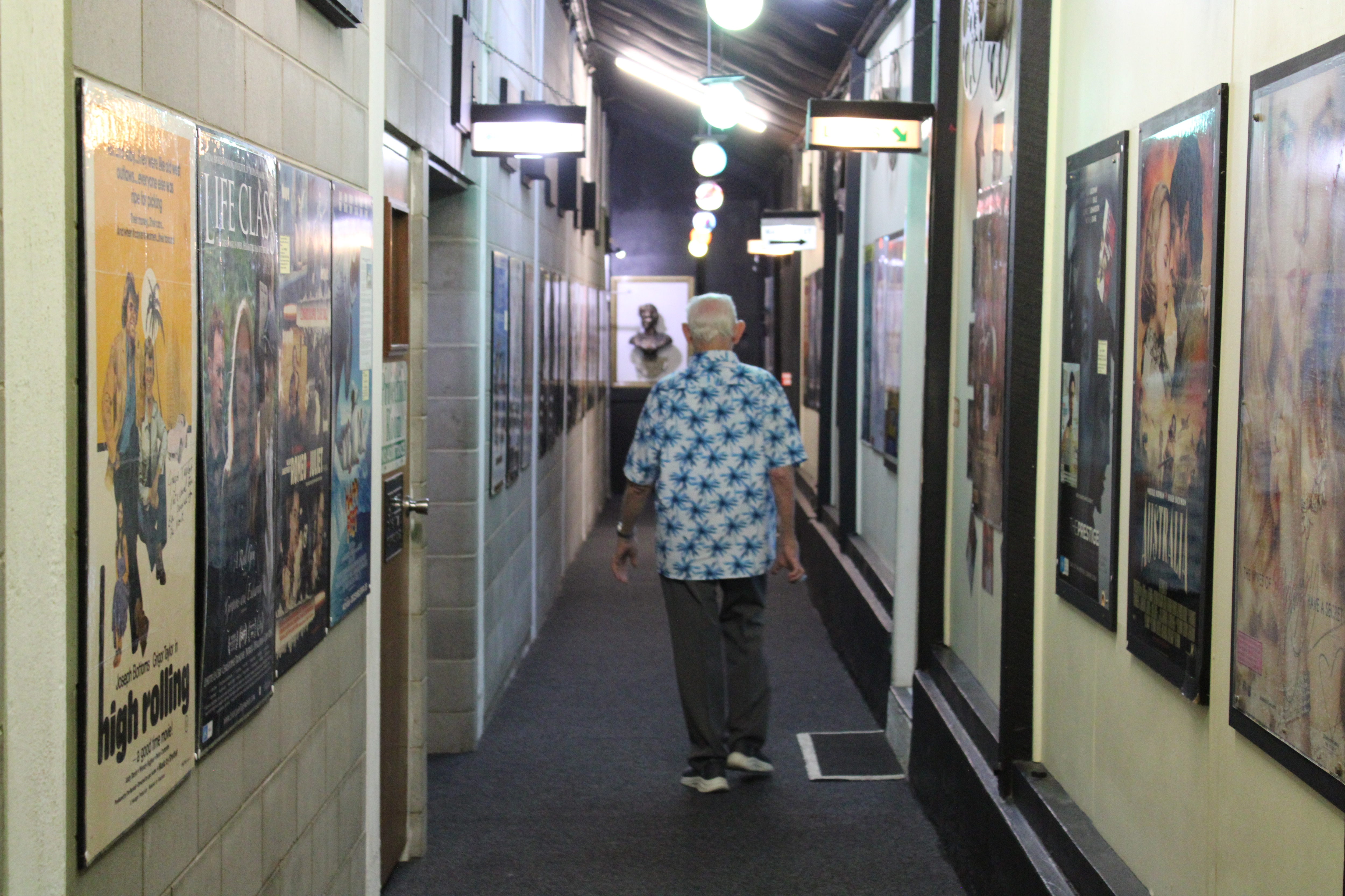 An elderly man in a blue tropical printed shirt standing in front of an old cinema.
