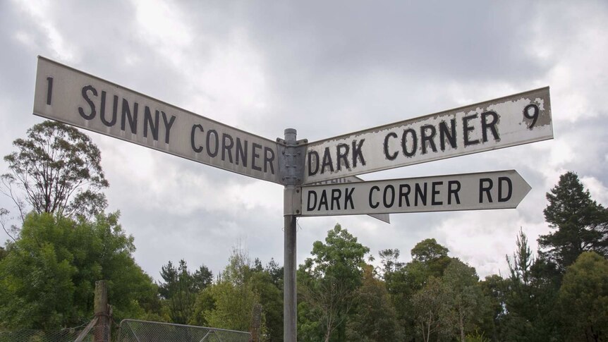 A road sign pointing in three ways to Sunny Corner, Dark Corner and Dark Corner Rd