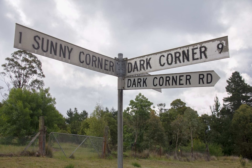 A road sign pointing in three ways to Sunny Corner, Dark Corner and Dark Corner Rd