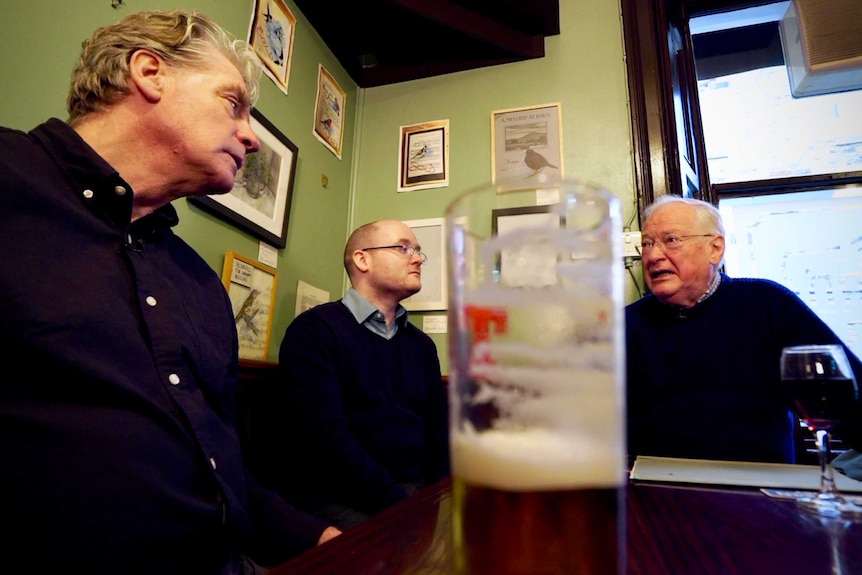 Three men sit at a table in a pub in Scotland.