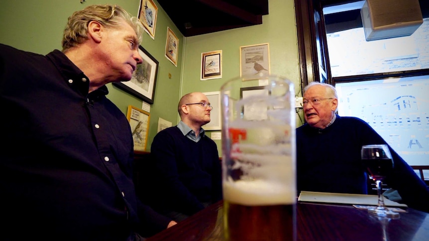 Three men sit at a table in a pub in Scotland.