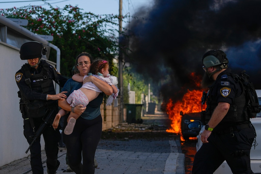 A woman carries a child past a fire 
