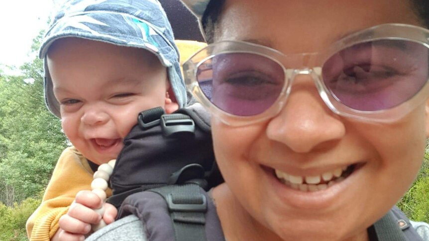 Lucille with her toddler son in a baby harness, both smiling, to depict supporting parents when baby is sick or has a disability