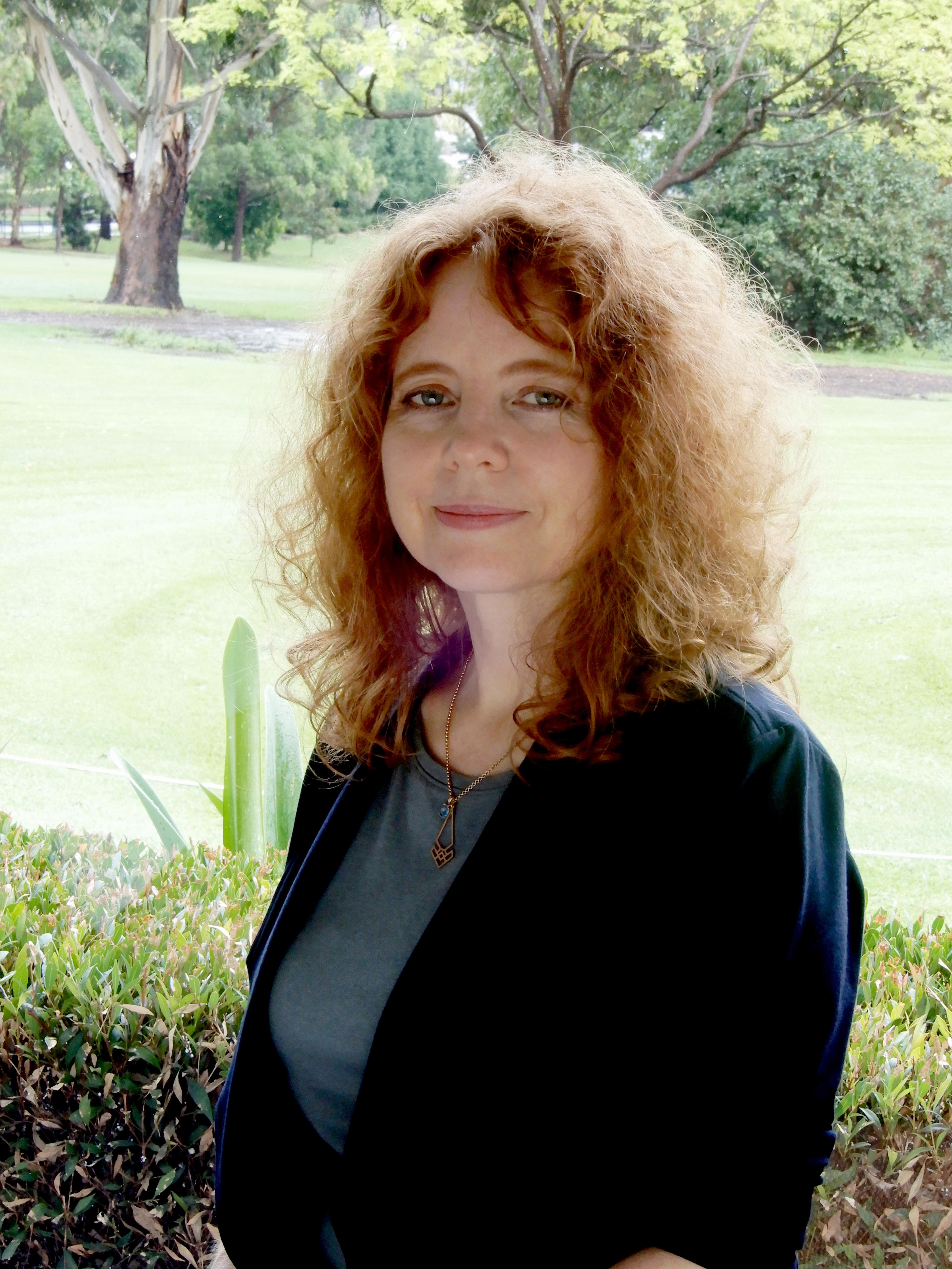 Portrait image of Dr Beth Cheal standing outside in front of trees and grass.