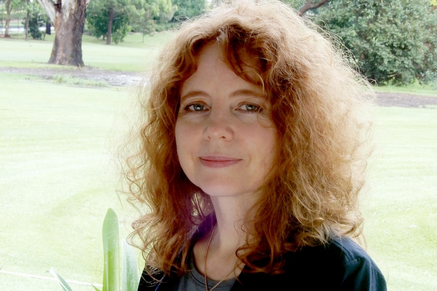 Portrait image of Dr Beth Cheal standing outside in front of trees and grass.