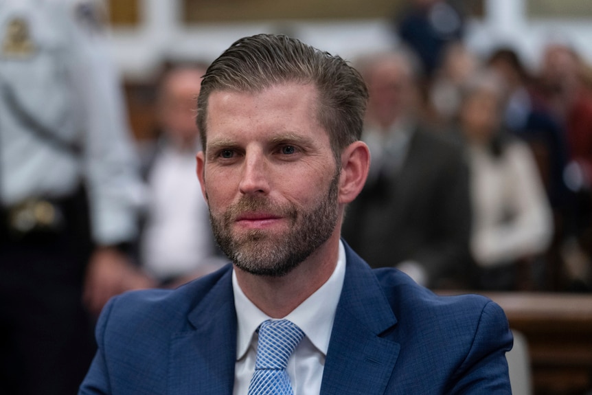 Eric Trump wearing a blue suit and a smile as he sits in a courtroom.