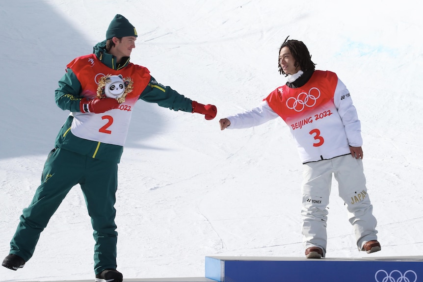 Two snowboard competitors standing on the podium, fist bumping.