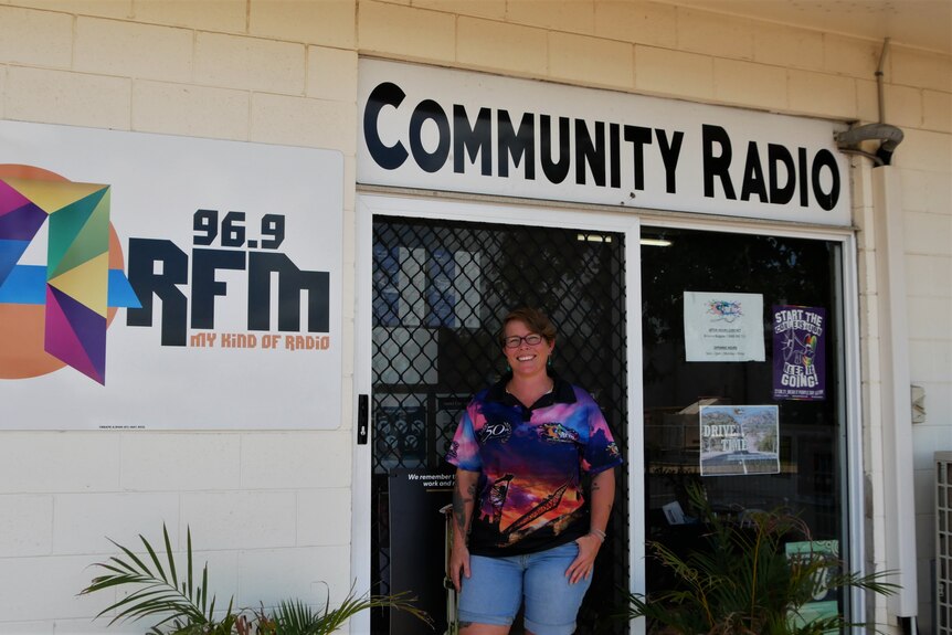 A woman stands outside a brick building with 'community radio' in large writing
