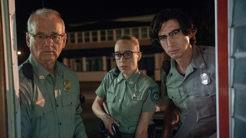 The three actors dressed in police uniforms looking towards camera as if through door. Sevigny holds gun; Driver holds machete.