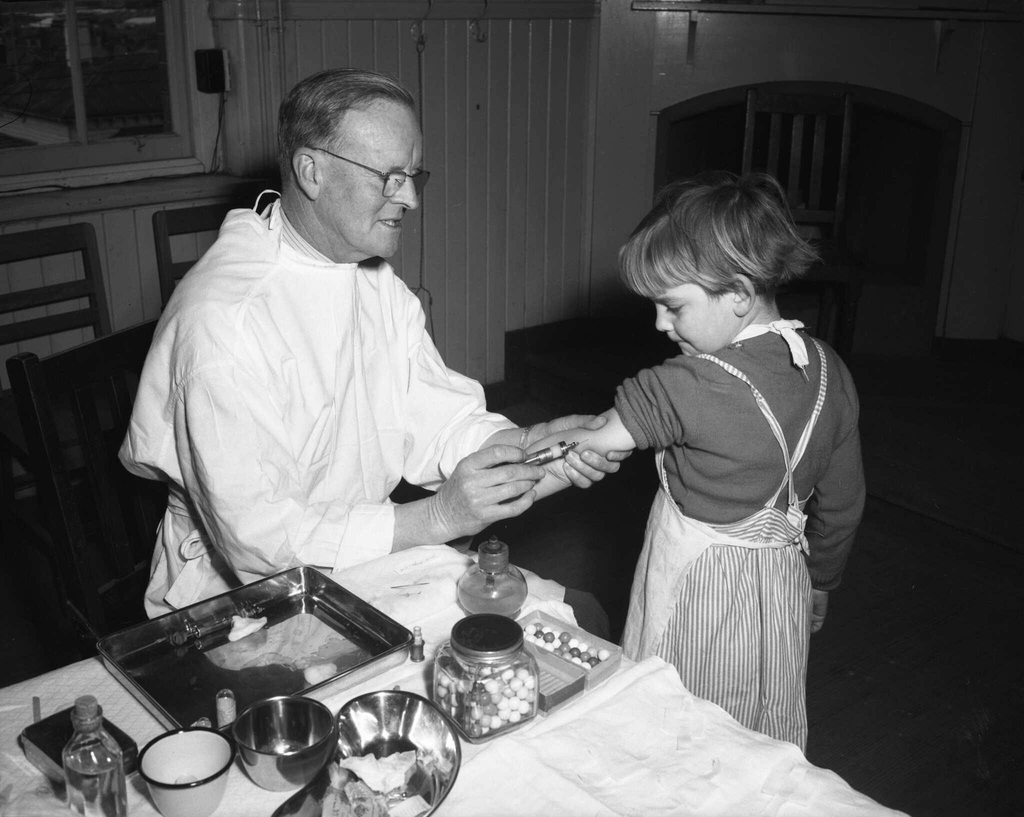 A young girl receives a vaccination from a man in a white coat in an undated black and white photograph.
