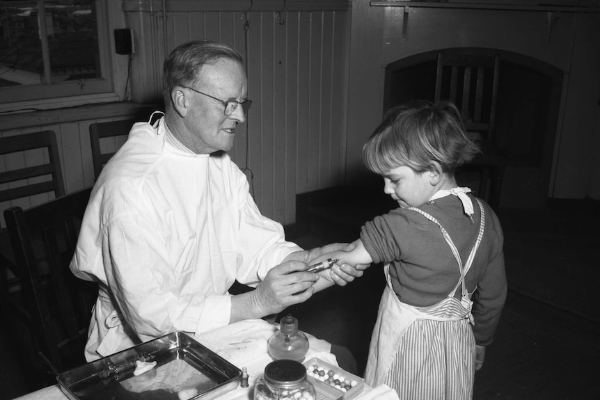 A young girl receives a vaccination from a man in a white coat in an undated black and white photograph.