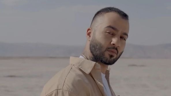 Head shot of Iranian man looking at the camera but body facing to the right with a desert background.