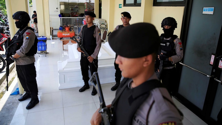 Armed policemen stands guard outside a door.