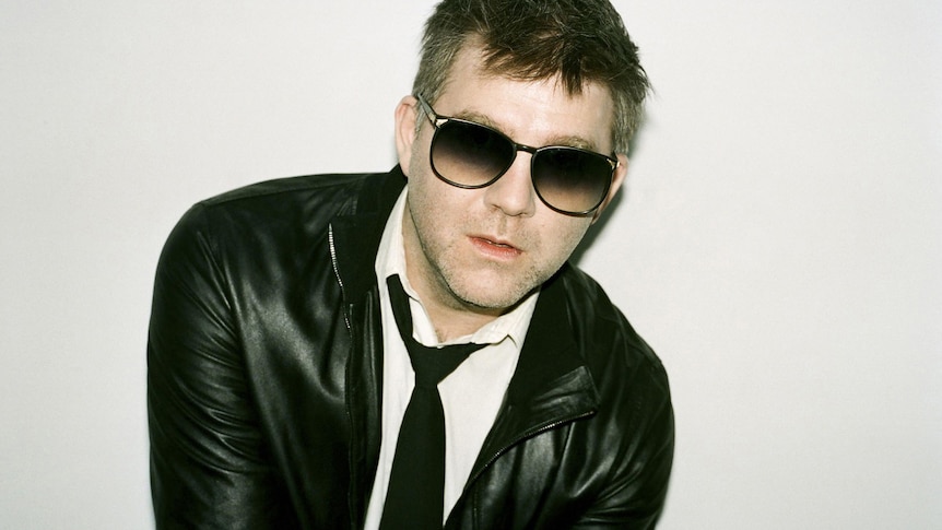 James Murphy of LCD Soundsystem wearing a black loosened tie, sunglasses and a leather jacket