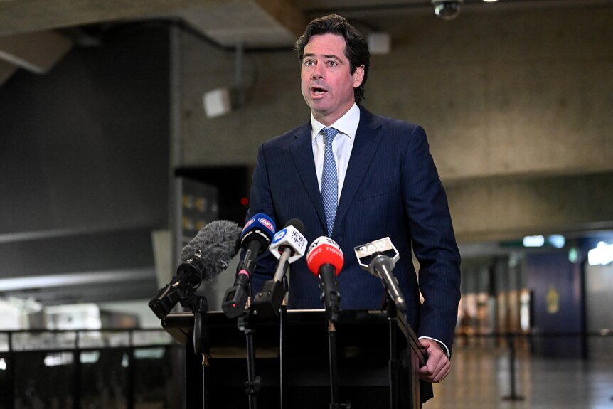 Gillon McLachlan speaks at a lecturn in front of microphones