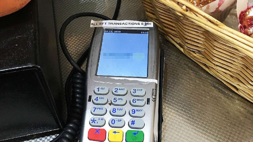 EFTPOS machine with a label saying all transactions attract a 25-cent surcharge