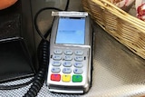 EFTPOS machine with a label saying all transactions attract a 25-cent surcharge